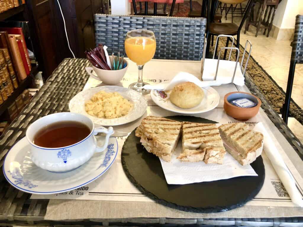 Portuguese breakfast with sandwiches, tea, orange juice, and bread on a table.